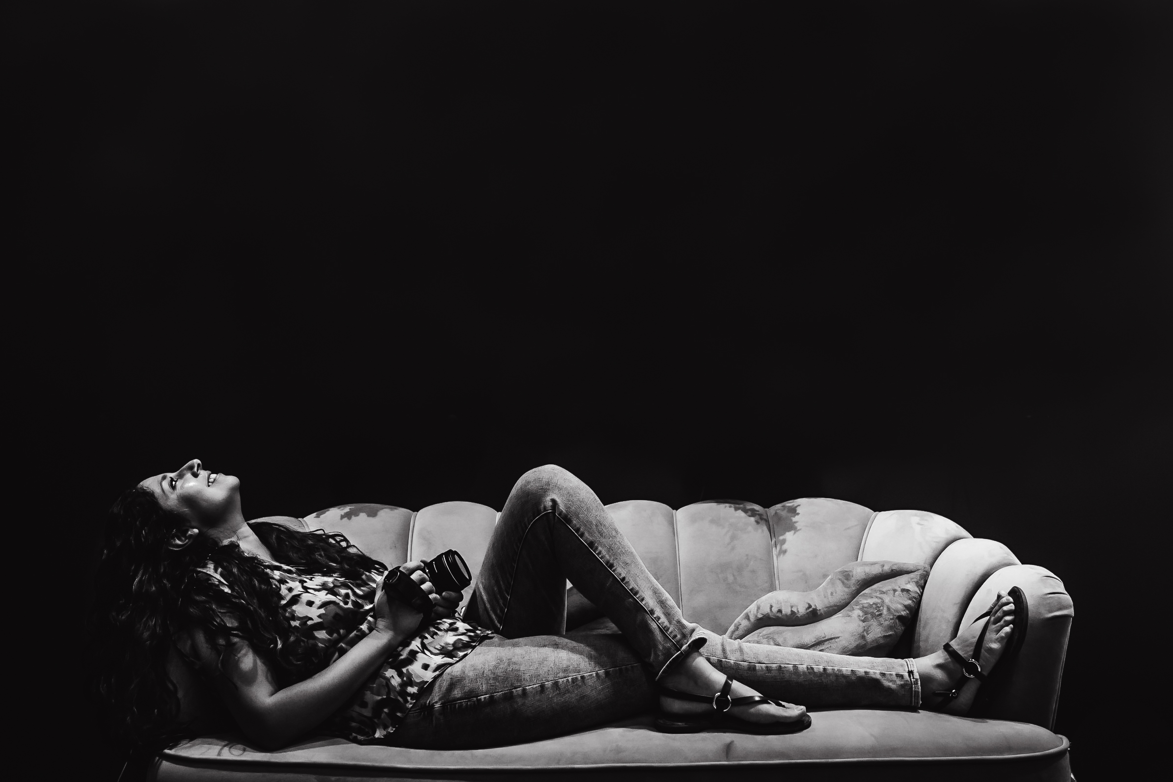 Black and white photo of Maribel laughing on a sofa with her camera