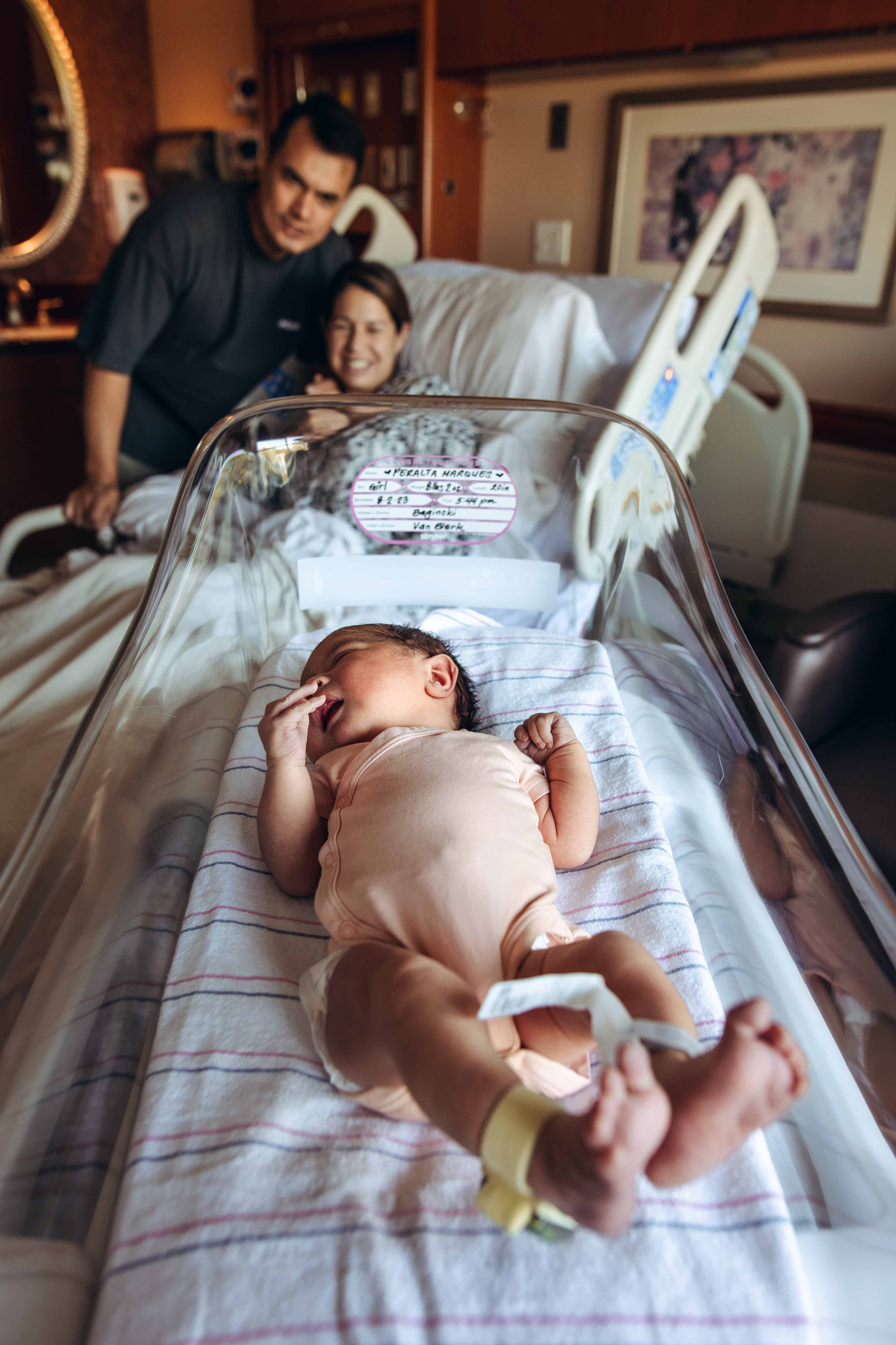 Newborn resting in the bassinet with parents watching over