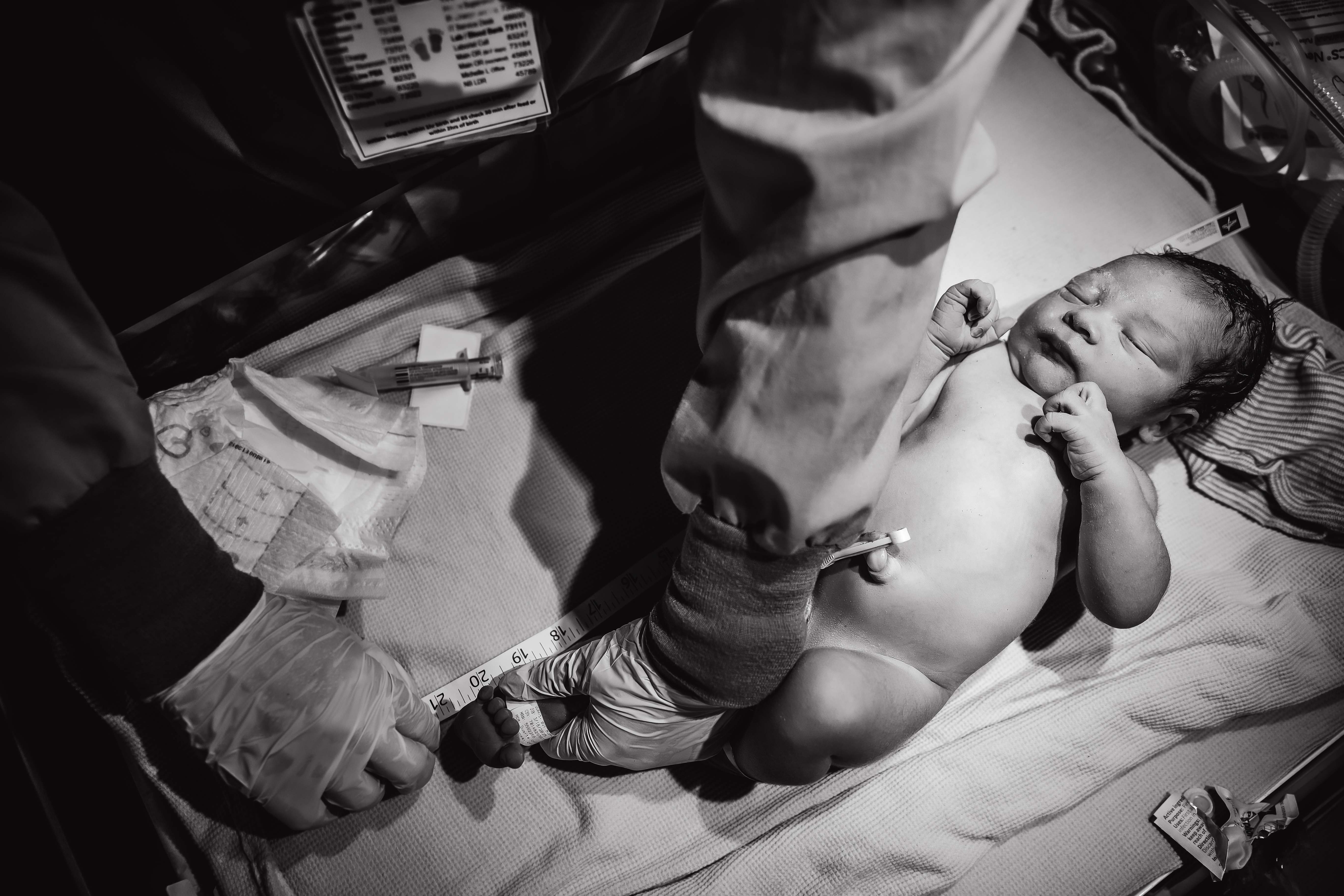 Dramatic black and white photo of a newborn being measured