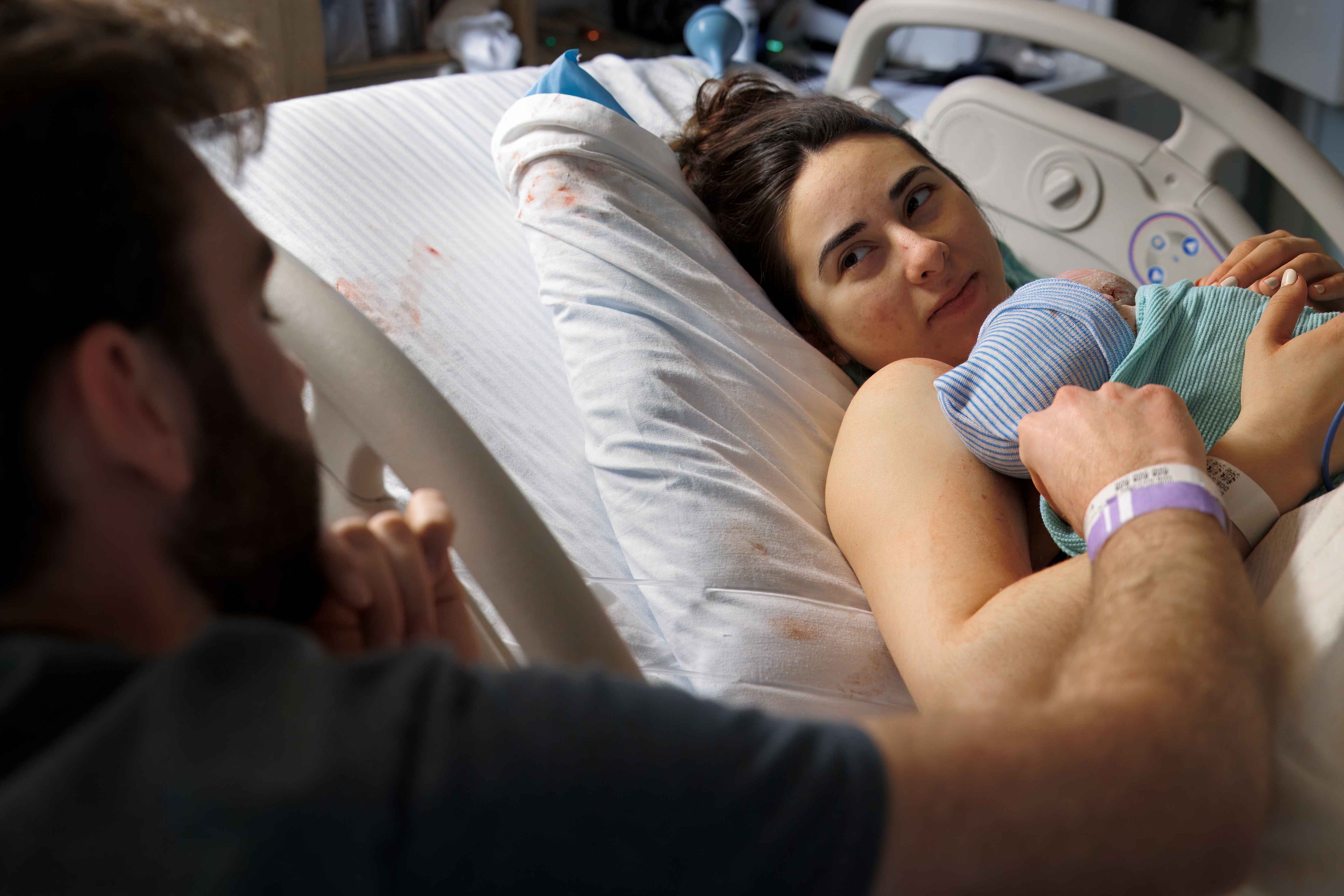 Mother in bed holding her newborn, gazing at her partner