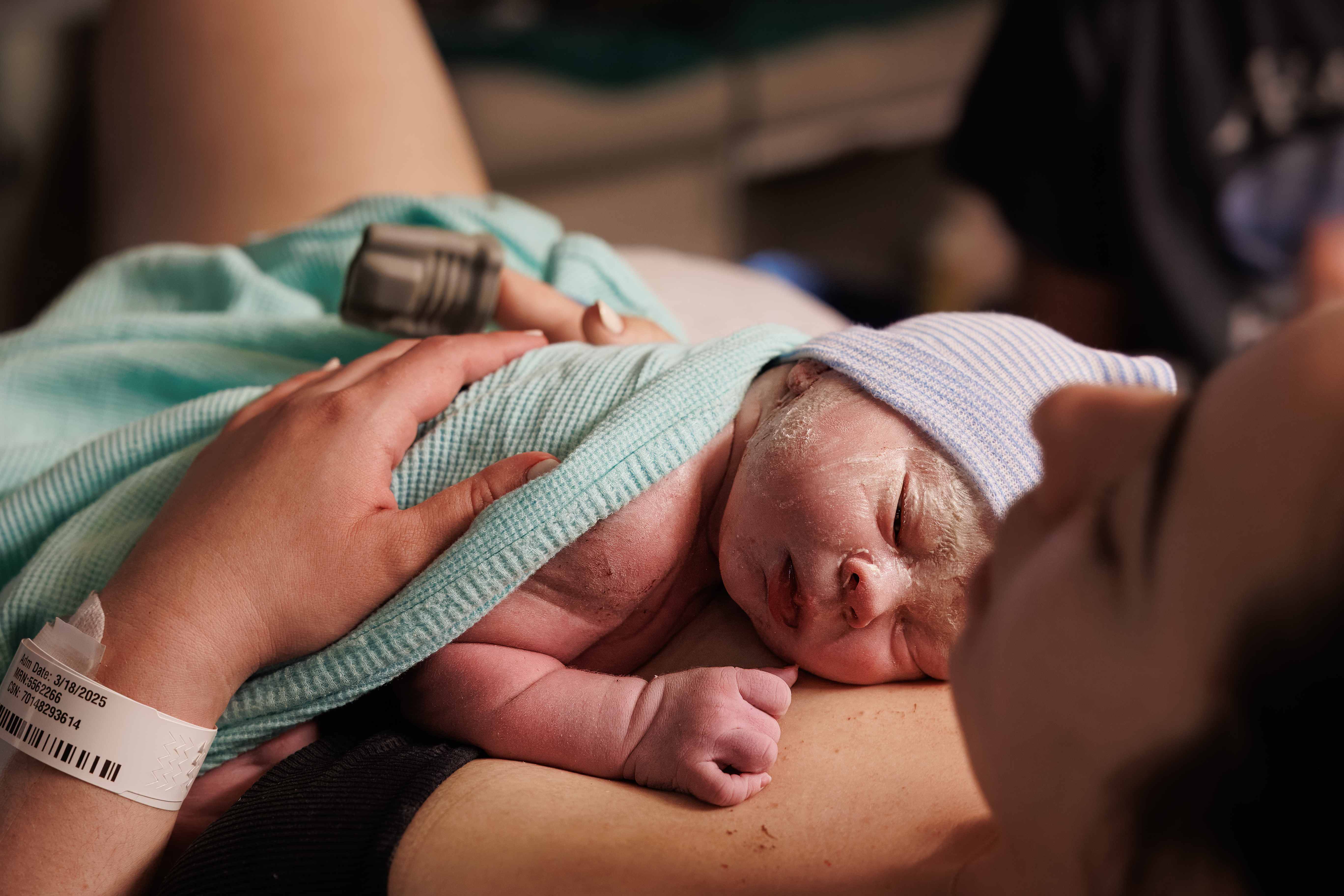 Newborn in a striped cap doing skin-to-skin on mother's chest