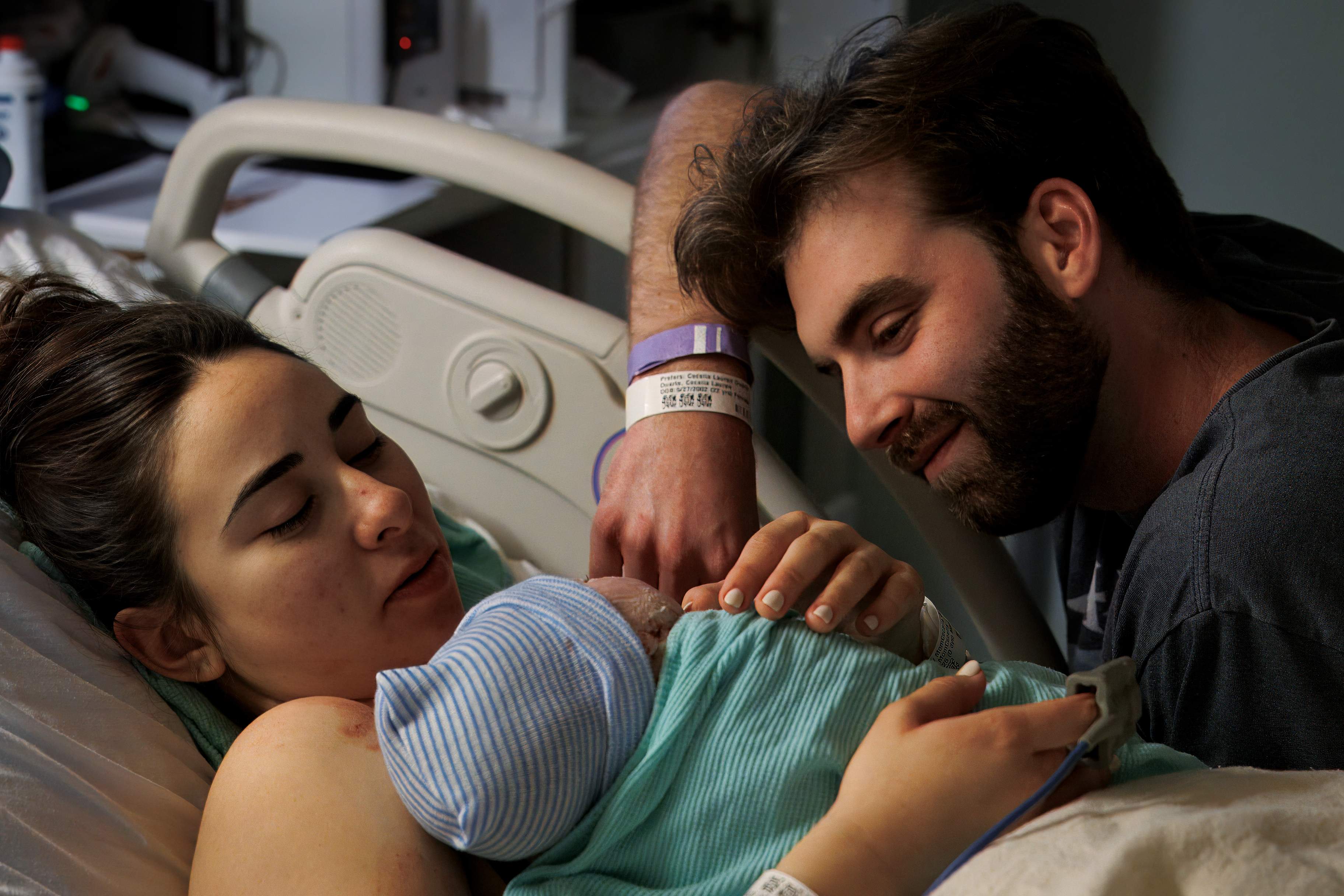 Mother resting with her newborn as her partner leans in tenderly