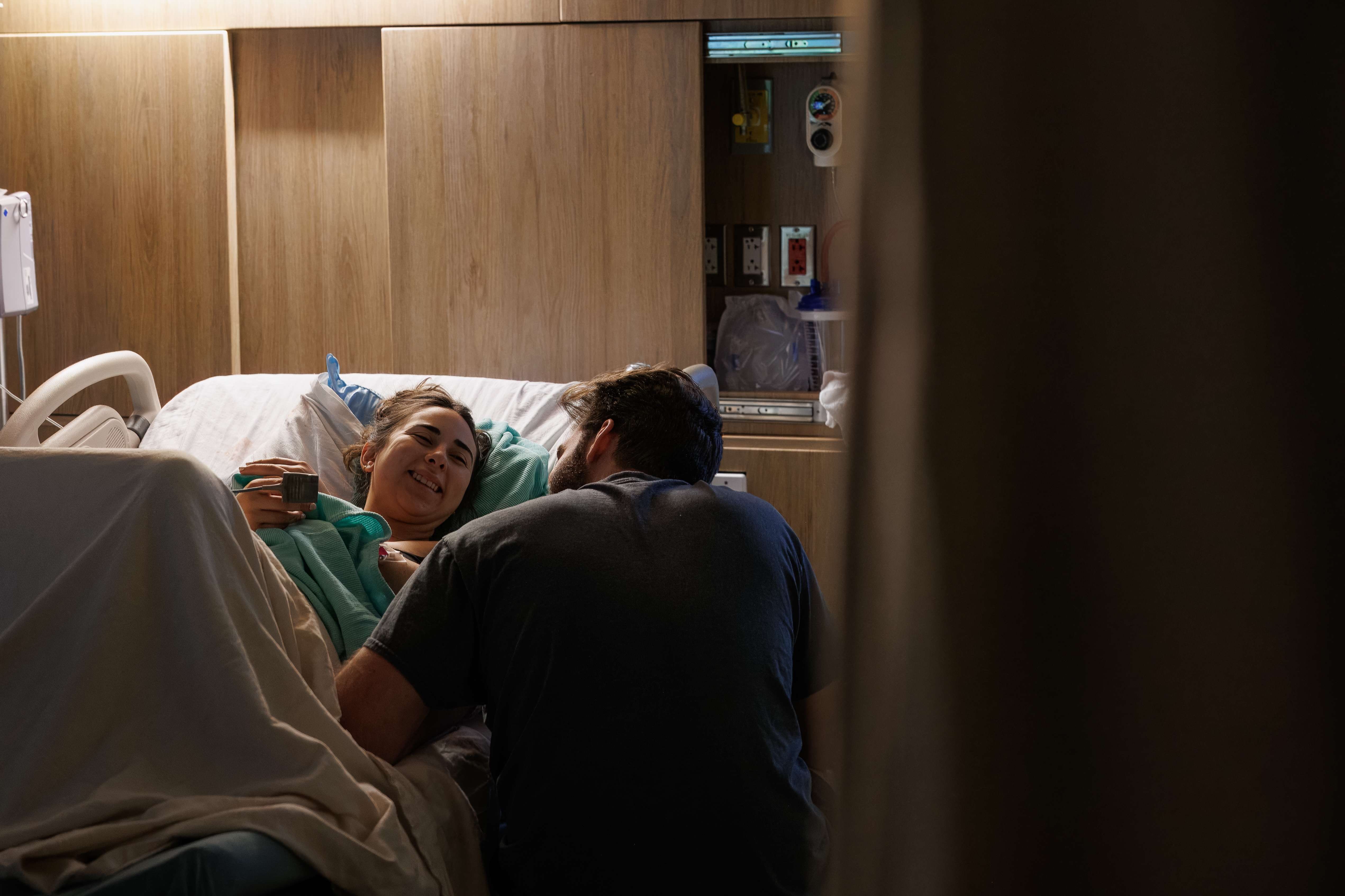 Mother laughing in bed as her partner leans close after birth
