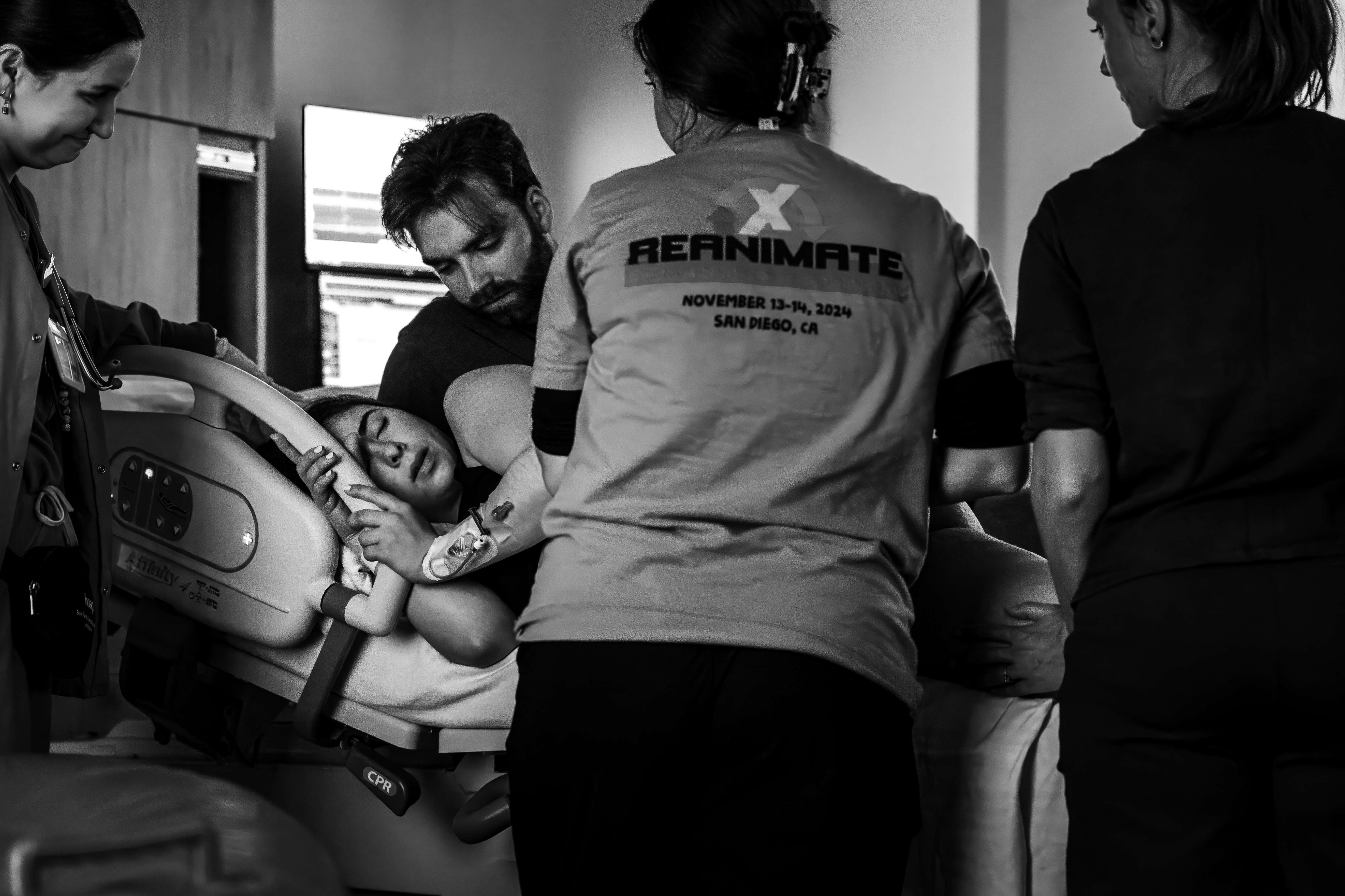 Black and white photo of a laboring mother supported by her partner and birth team