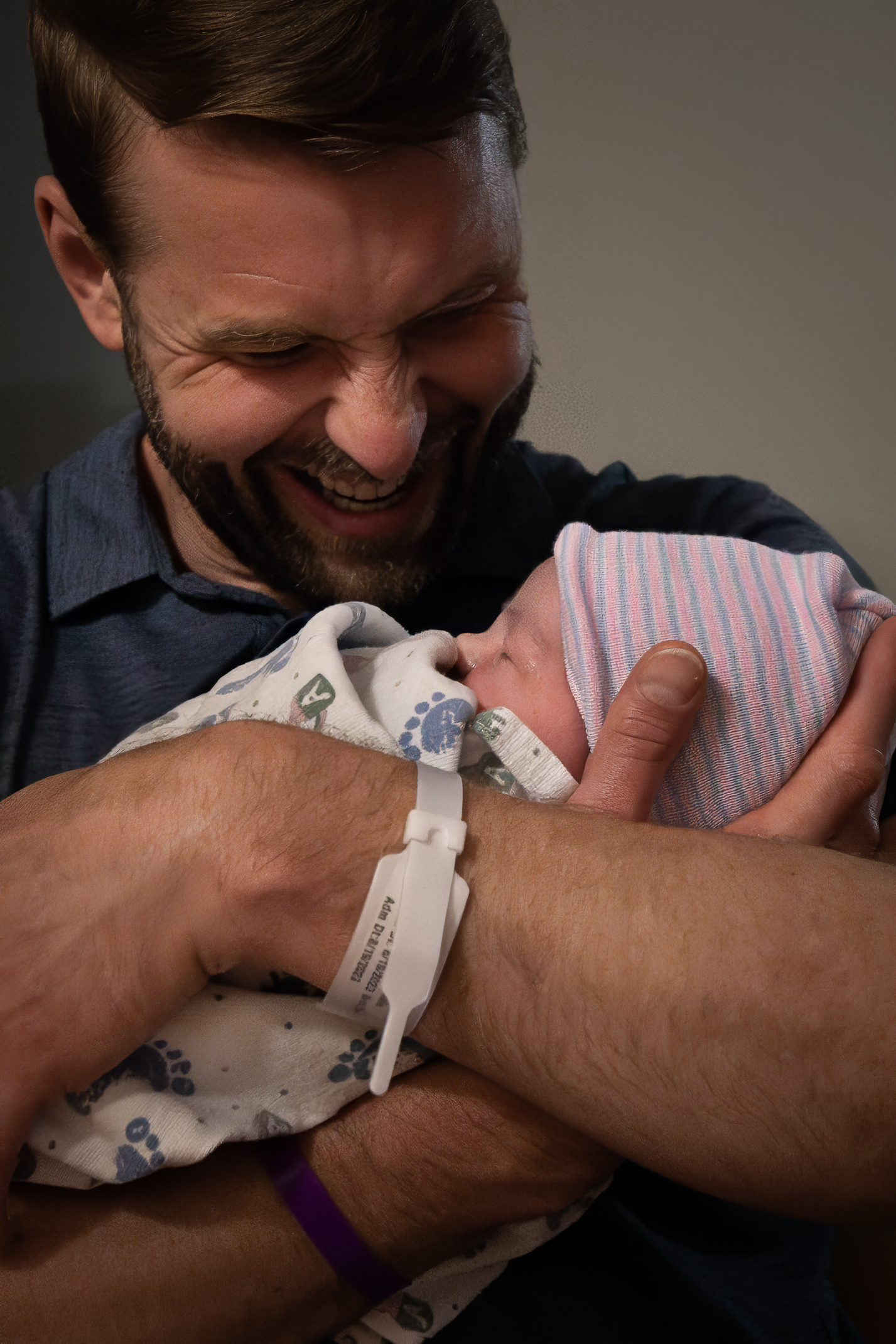 A father beaming down at his newborn in a striped hospital hat