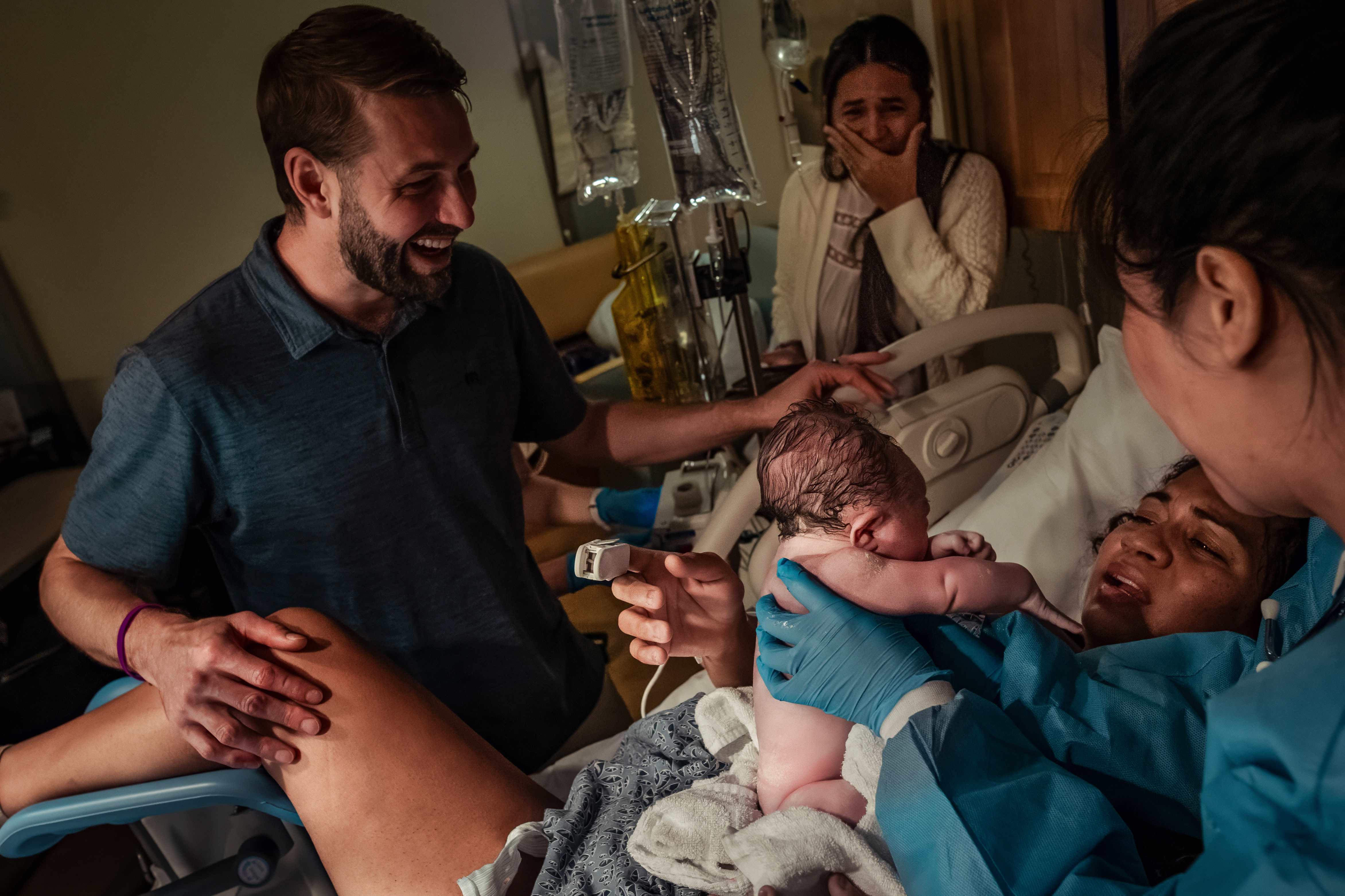 The moment of birth as the baby arrives, with family and grandmother nearby
