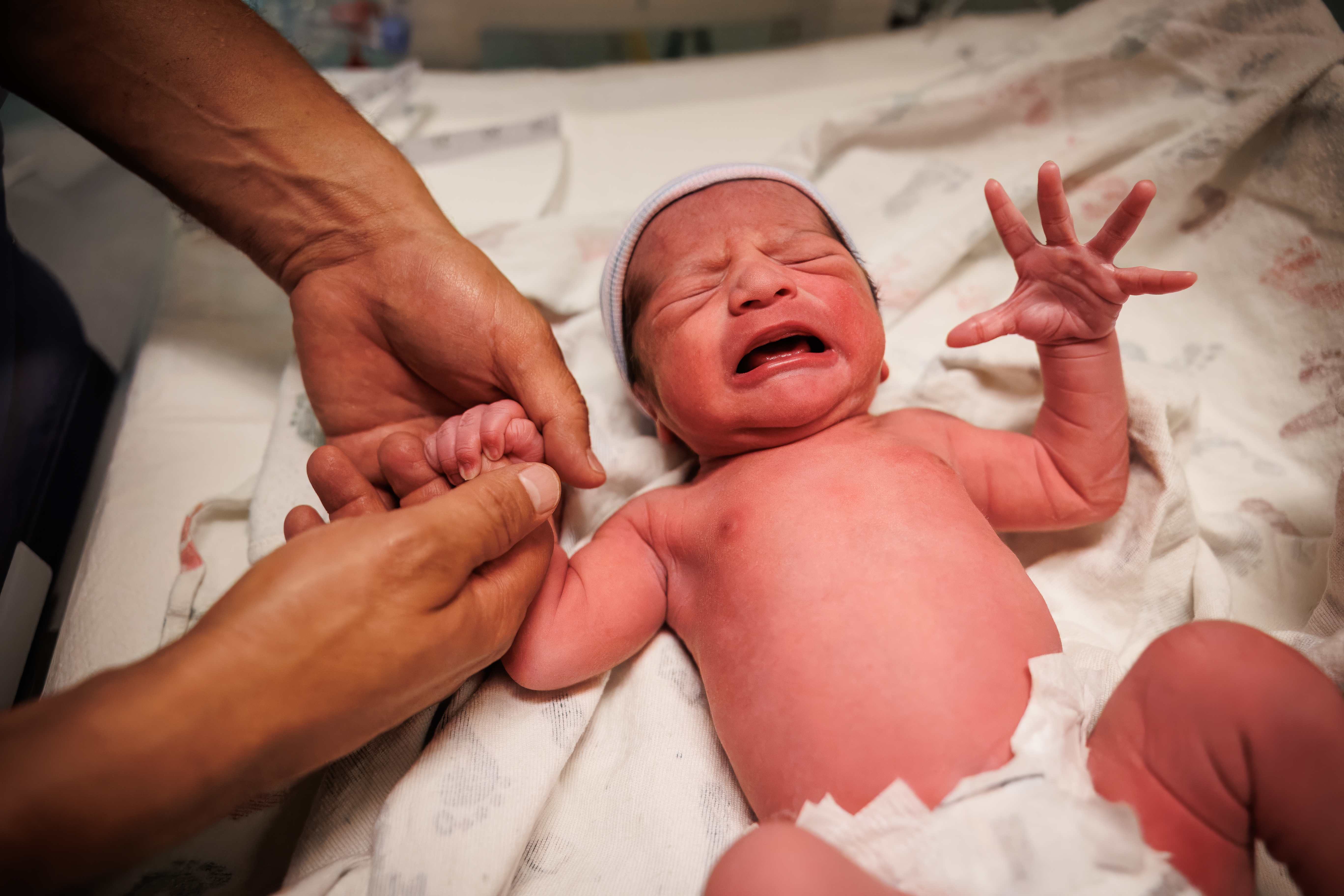 A newborn crying moments after birth, held in loving hands