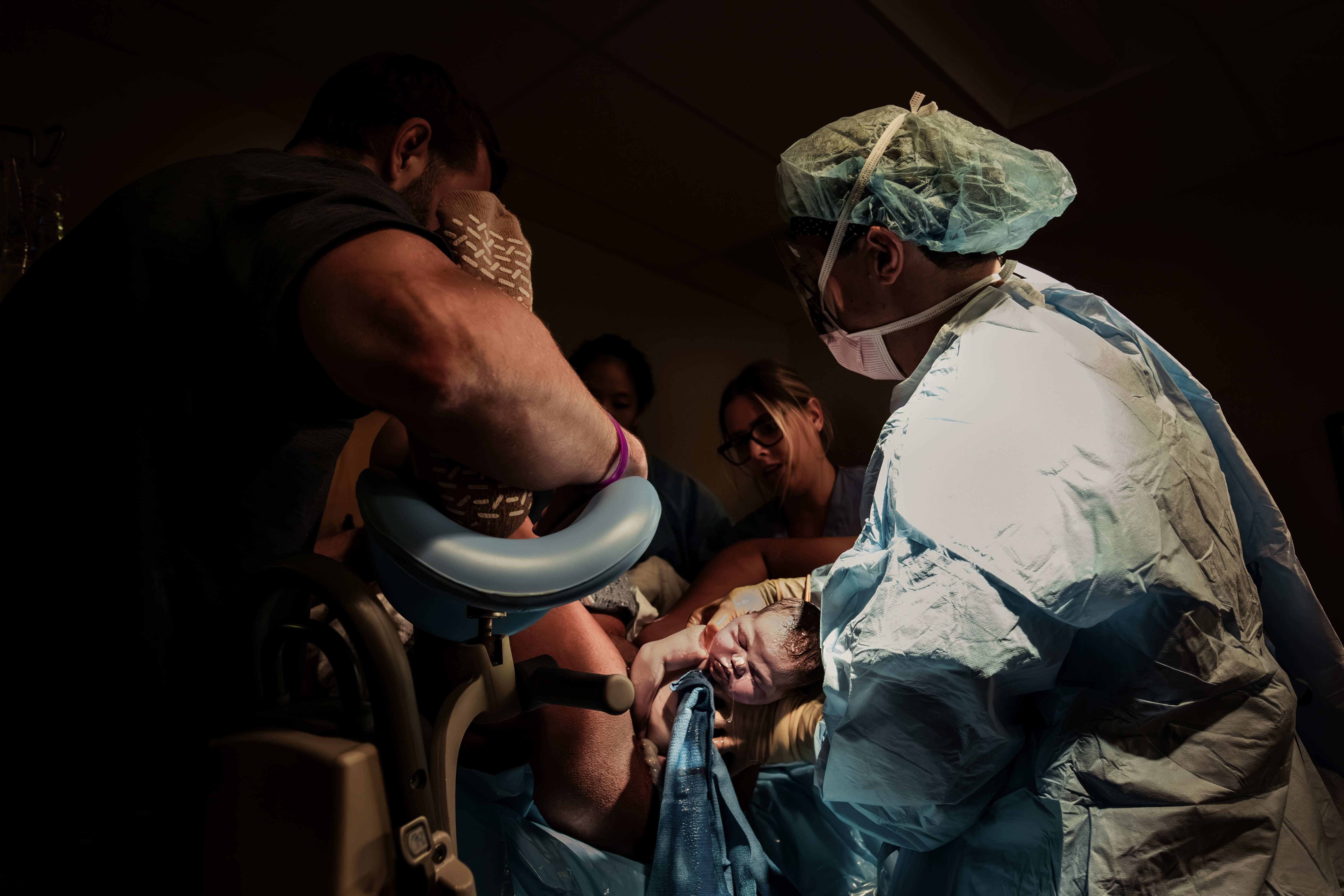 A baby being born as the provider and partner support the mother